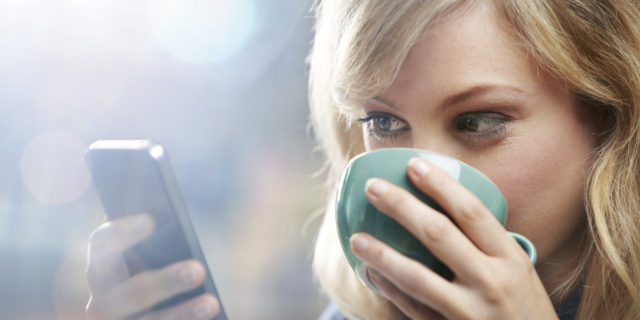 Woman using phone and drinking coffee.